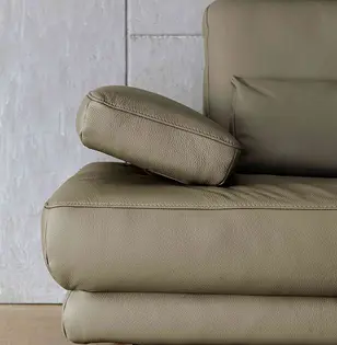 Detailansicht eines olivgrünen Ledersofas mit weich gepolsterter Armlehne und feiner Ziernaht. Hochwertige Verarbeitung und sanfte Rundungen betonen Komfort und elegantes Design vor schlichter Wand.